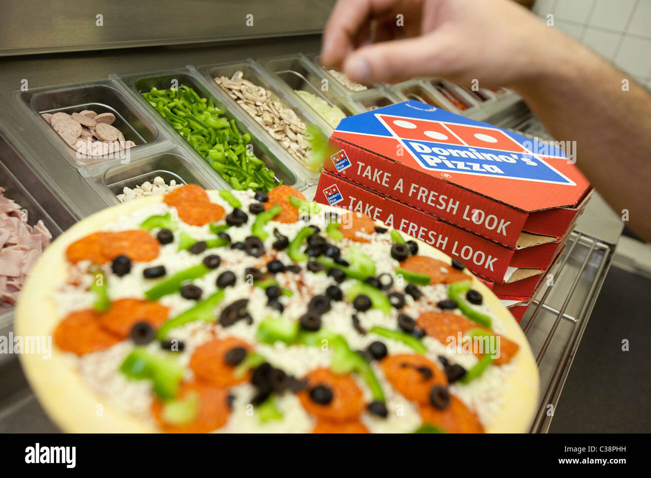 A Domino's Pizza employee preparing a fresh pizza ready for the cooking oven. Stock Photo