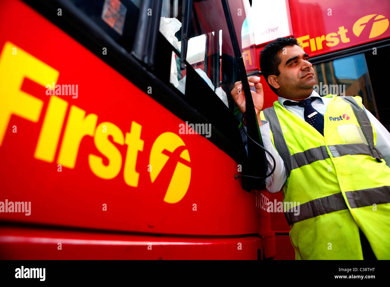 A First Group bus driver in a high visibility vest with two First Group buses at Aldgate bus station, Central London. Stock Photo