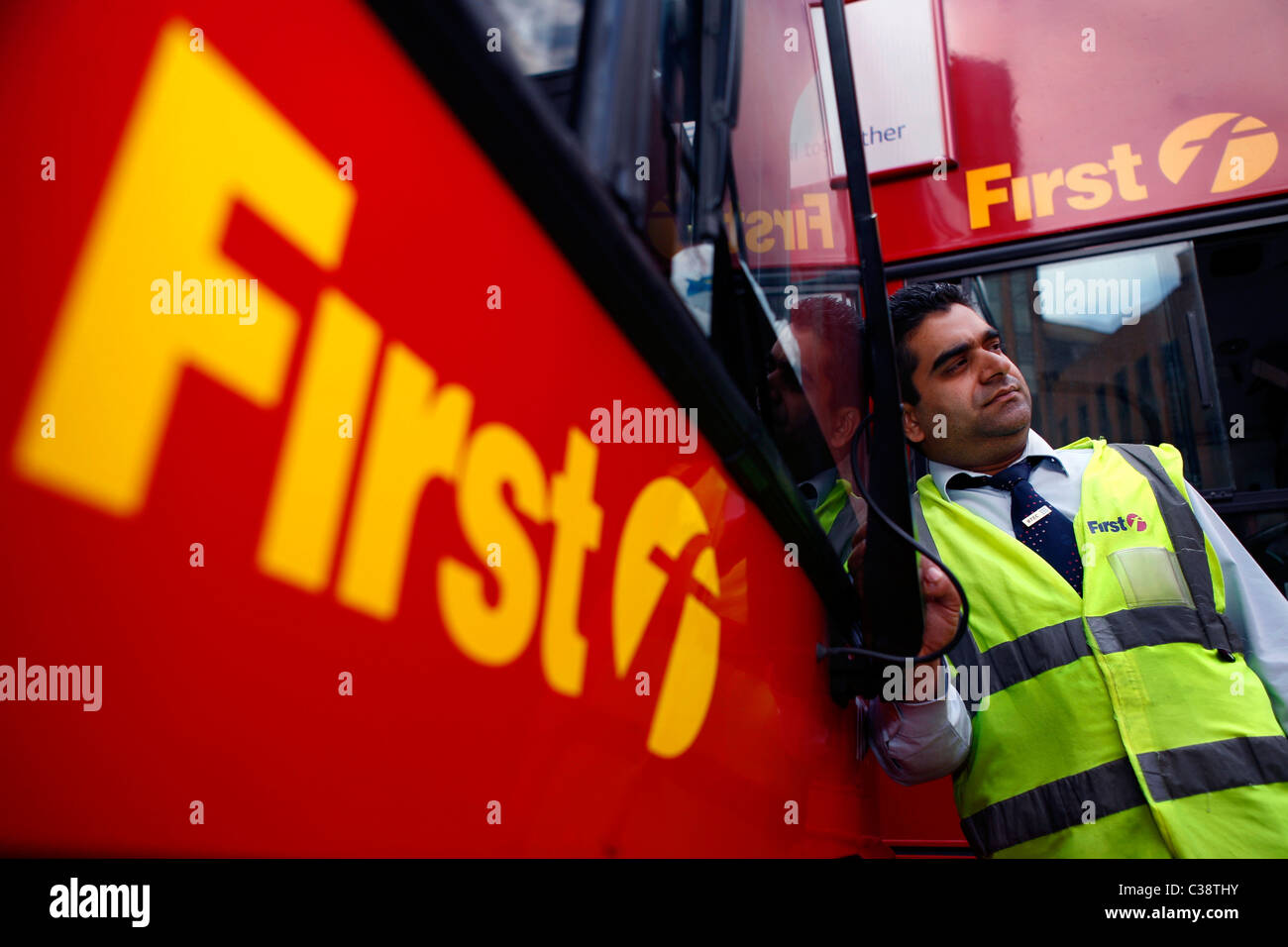 A First Group bus driver in a high visibility vest with two First Group buses at Aldgate bus station, Central London. Stock Photo