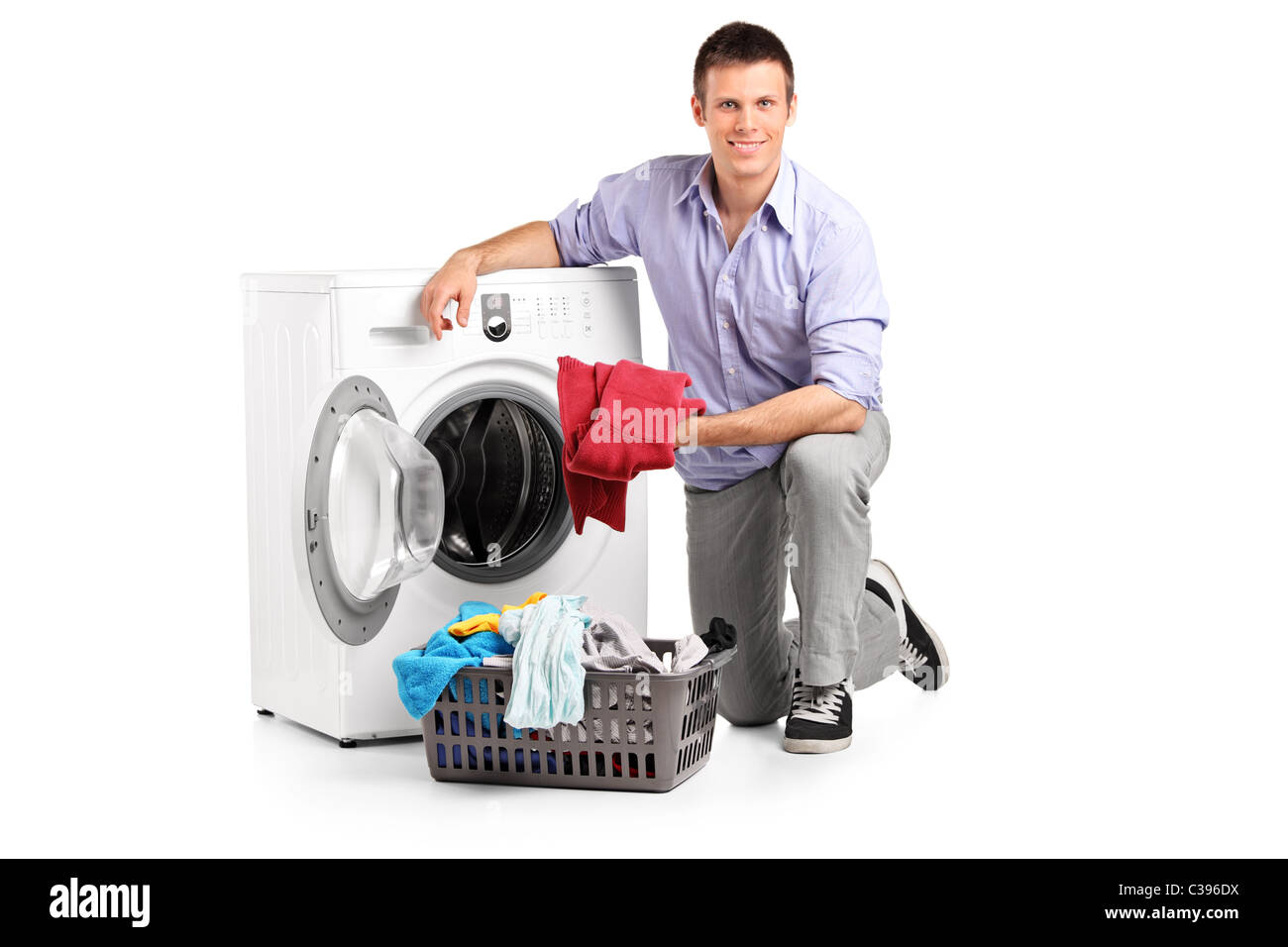 Young man putting clothes into washing machine and smiling Stock Photo