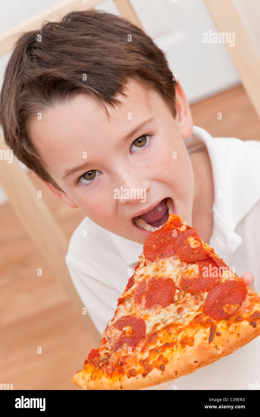 A young boy child eating a slice of pepperoni and cheese pizza Stock