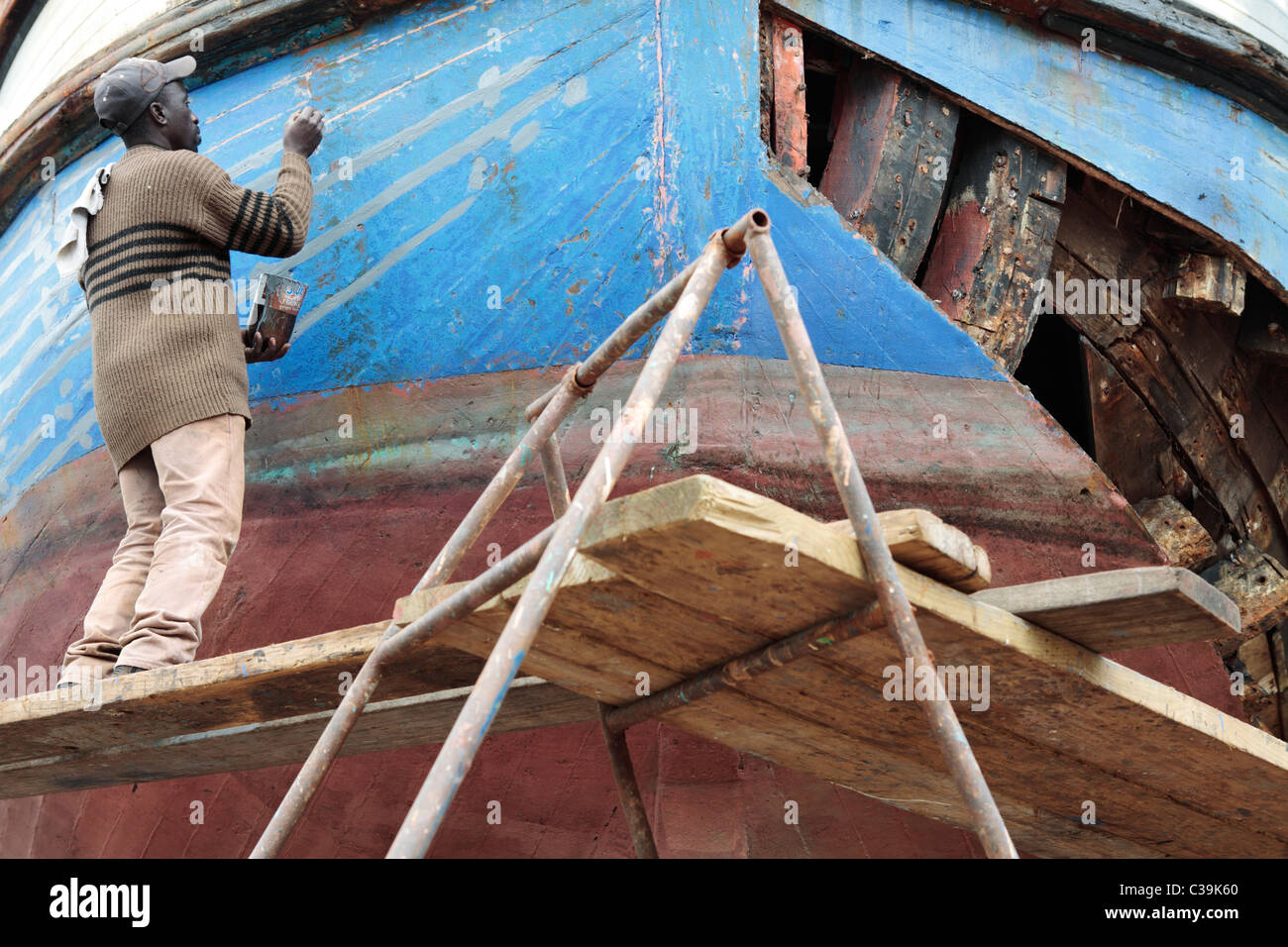 Workman painting repaired hull of wooden fishing boat in a ...