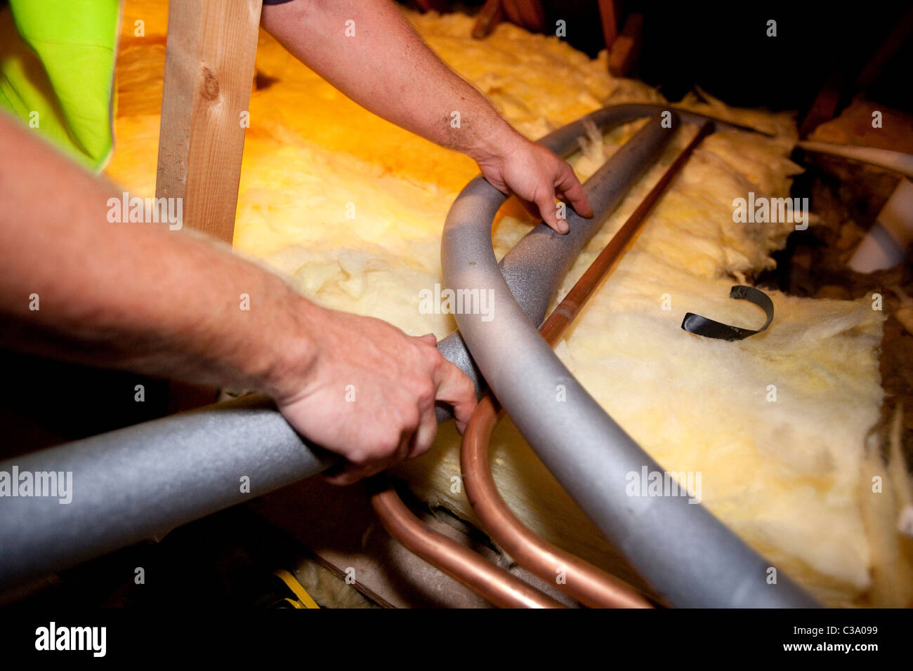 loft insulation. A worker from Total Insulation Solutions lags water pipes in a loft Stock Photo