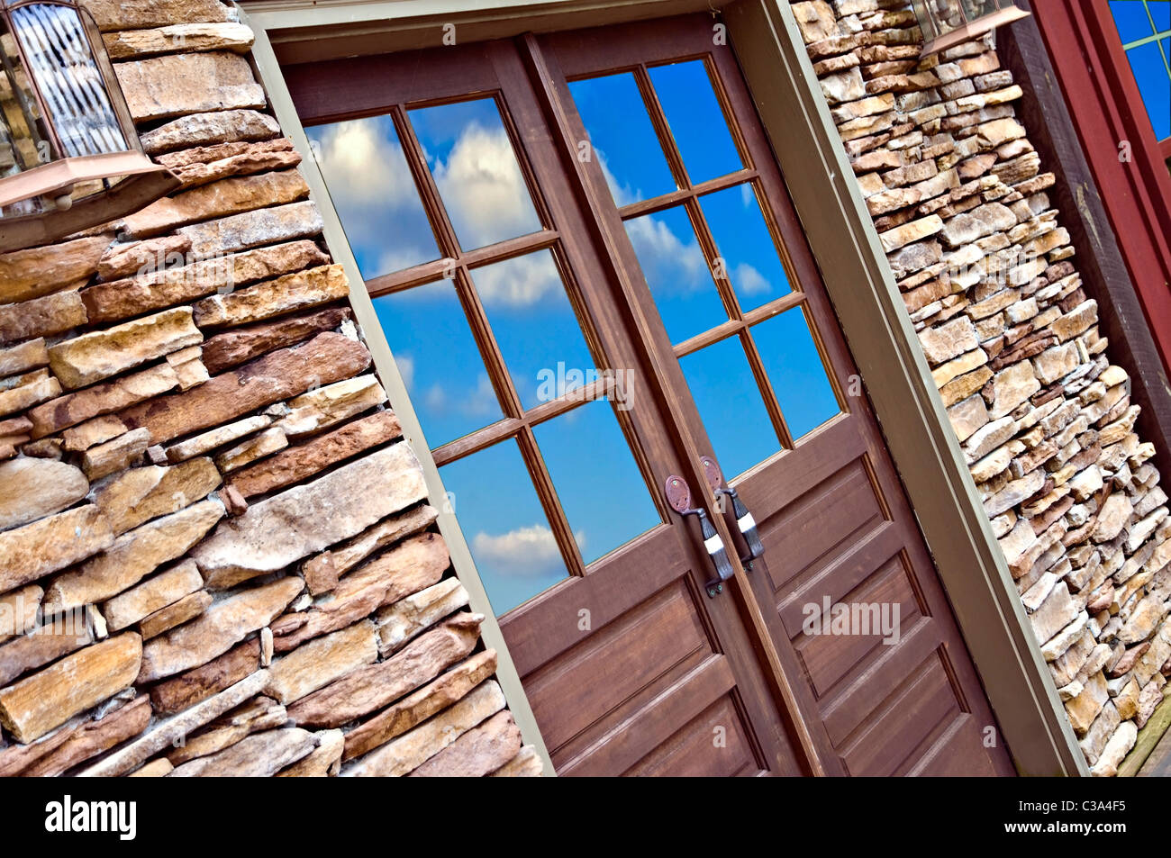 Wooden door in a rock wall with reflection of sky and clouds. Stock Photo