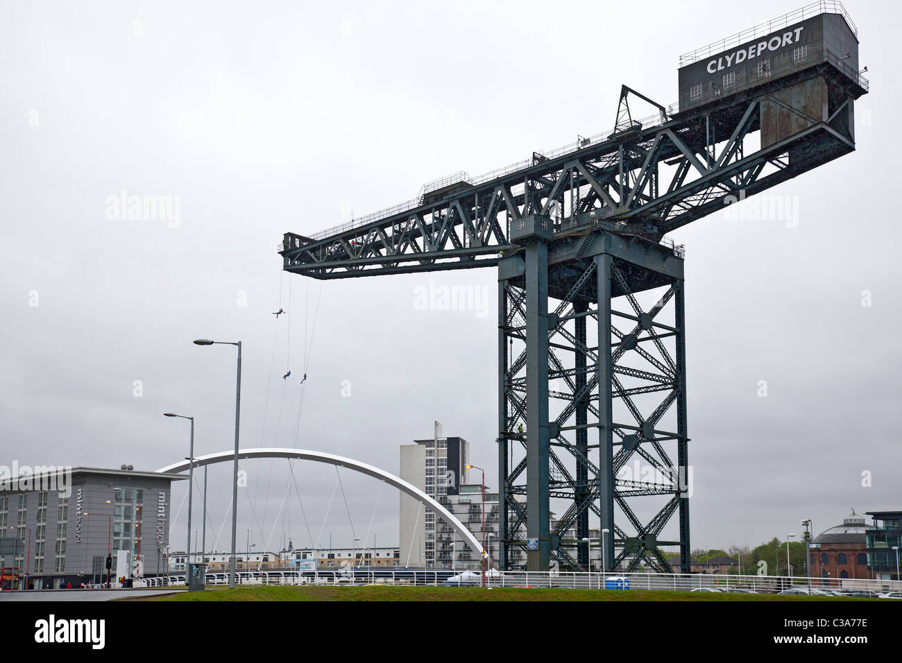 Three people complete a charity abseil from the Finnieston Crane, Glasgow, in front of the Clyde Arc bridge. Scotland, UK. Stock Photo