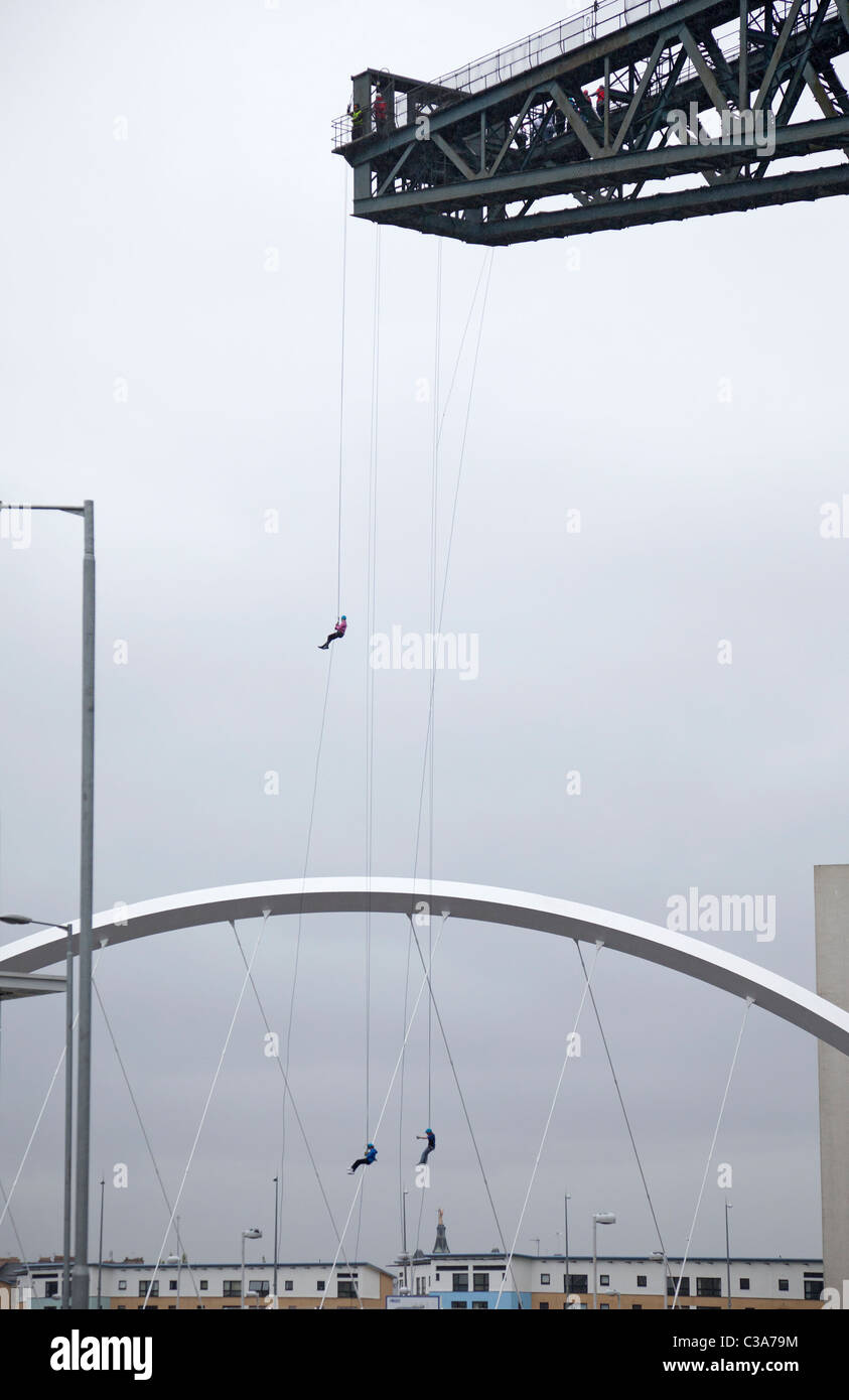 Three people complete a charity abseil from the Finnieston Crane, Glasgow, in front of the Clyde Arc bridge. Scotland, UK. Stock Photo