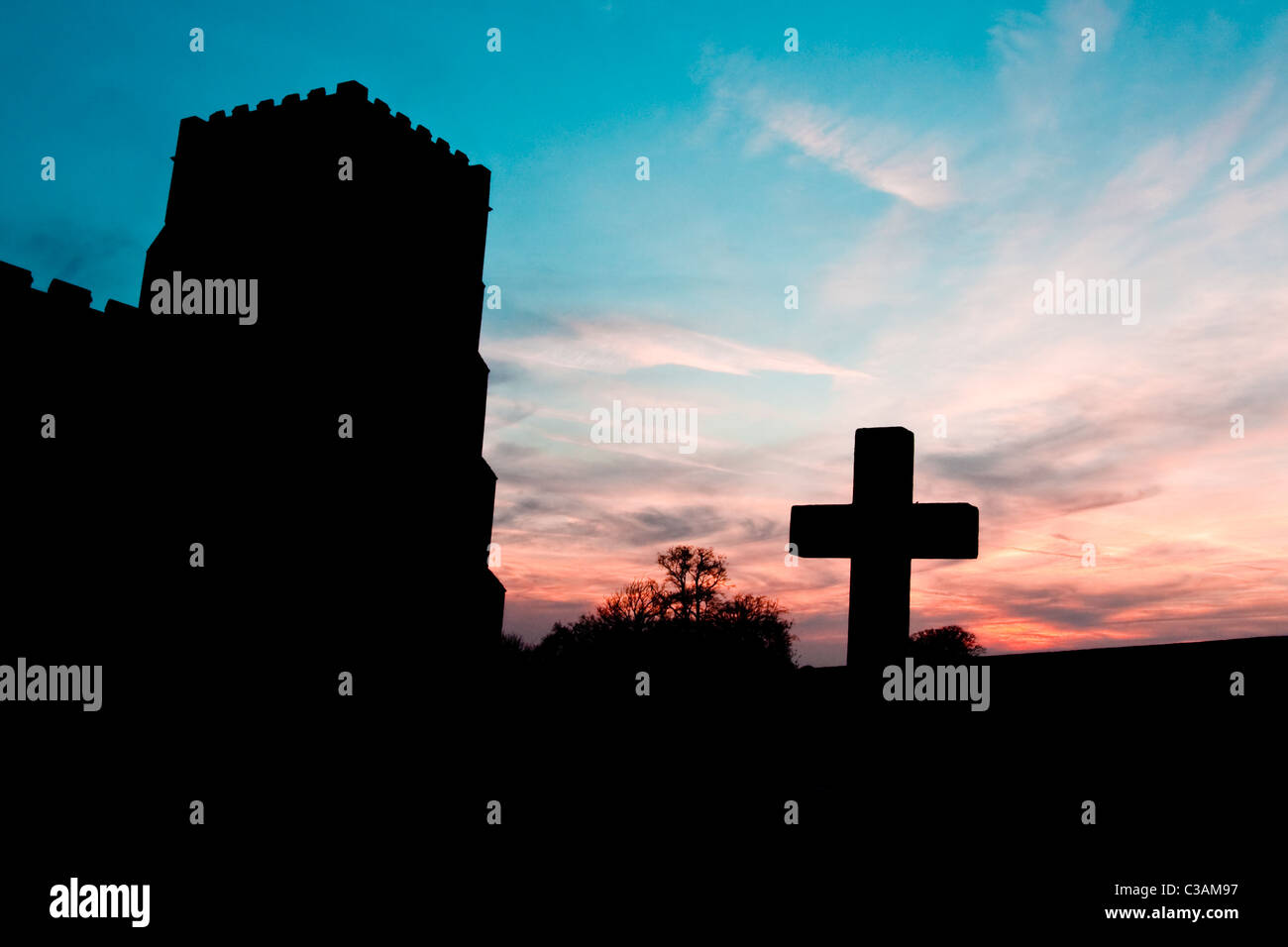 Silhouette of a cross against a colorful sky at dusk in the churchyard of St Mary's at Dalham in Suffolk Stock Photo