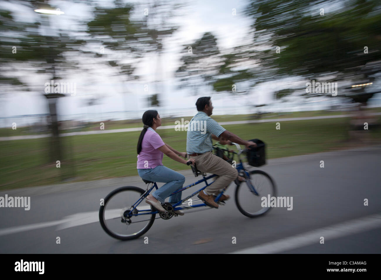 two blurry figures ride a tandem bicycle in east coast park, Singapore