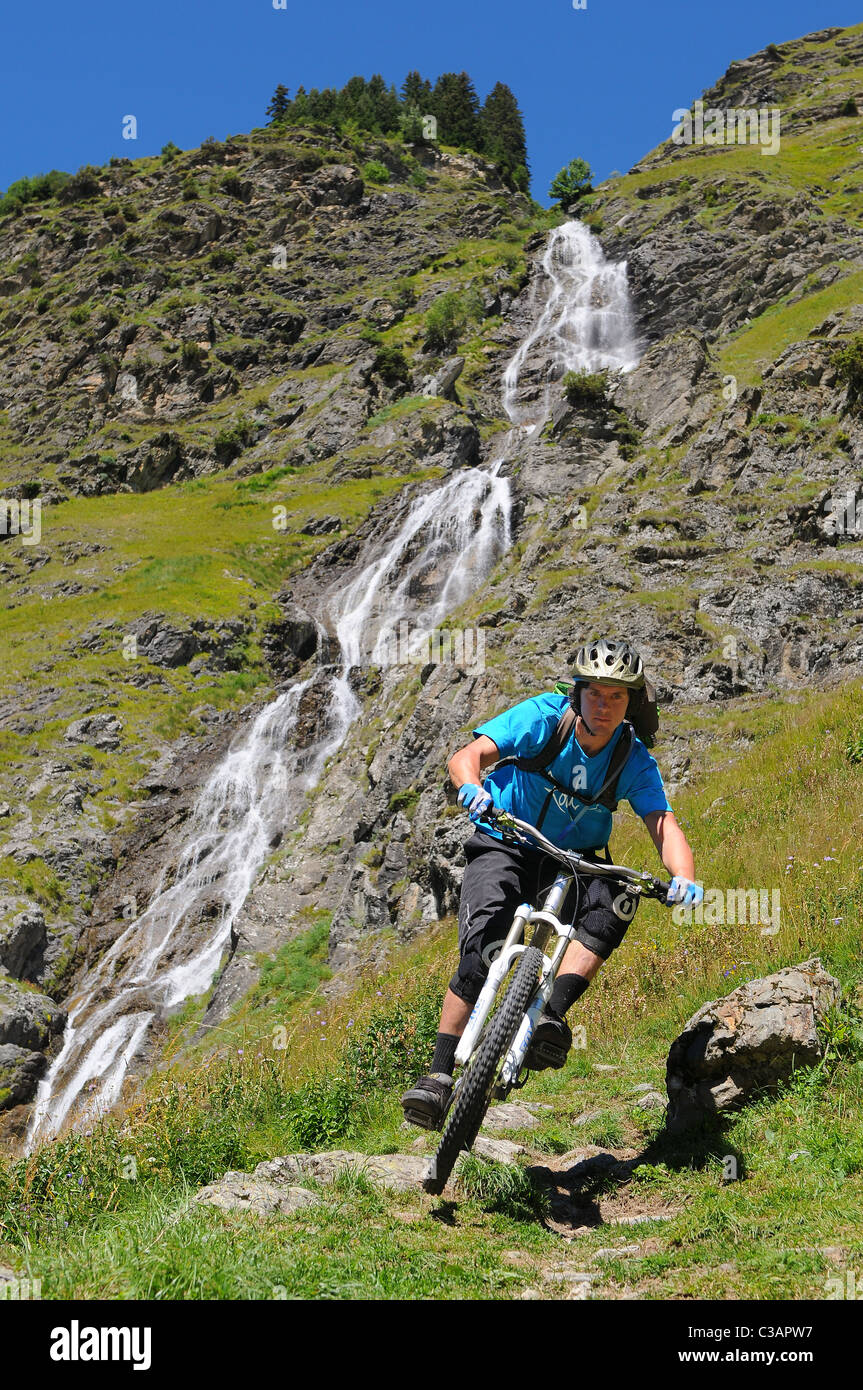 A mountain biker turns a corner on a steep mountain path next to a waterfall above the town of Champagny en Vanoise in France. Stock Photo