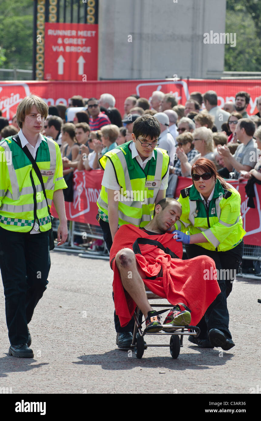 Collapsed competitor helped away  by St John Ambulance in London marathon 2011  watched by crowds. Medical attention. Stock Photo