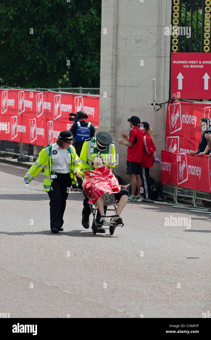 Collapsed competitor helped away  by St John Ambulance in London marathon watched by crowds. Medical attention. 2011 Stock Photo