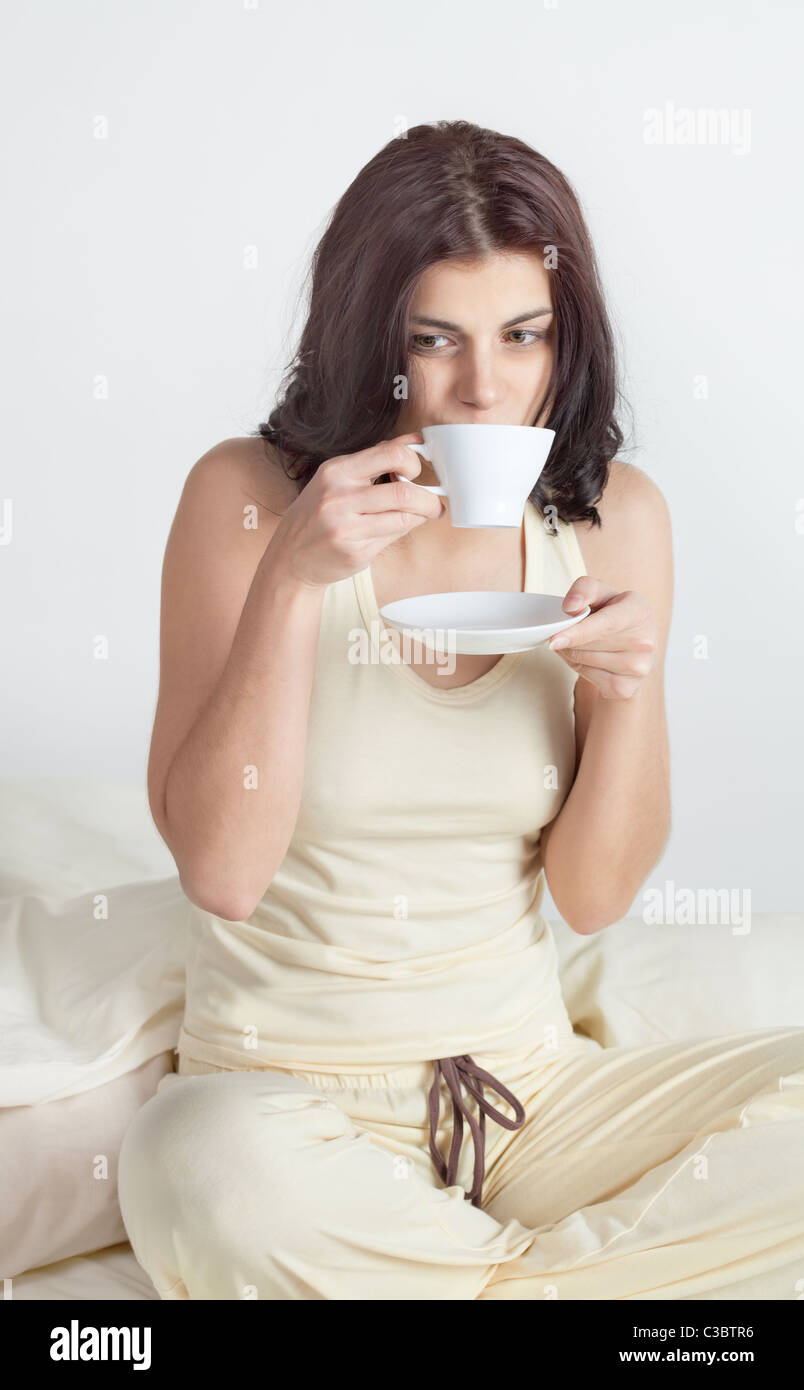 Young woman in bed holding a cup of coffee after she waken up Stock Photo