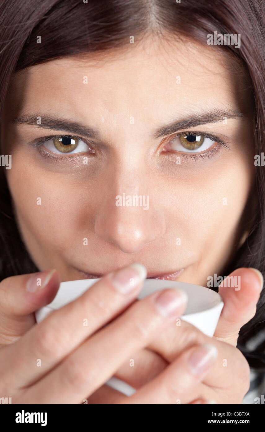 Closeup portrait of young brunette woman holding a cup of coffee close to her lips Stock Photo