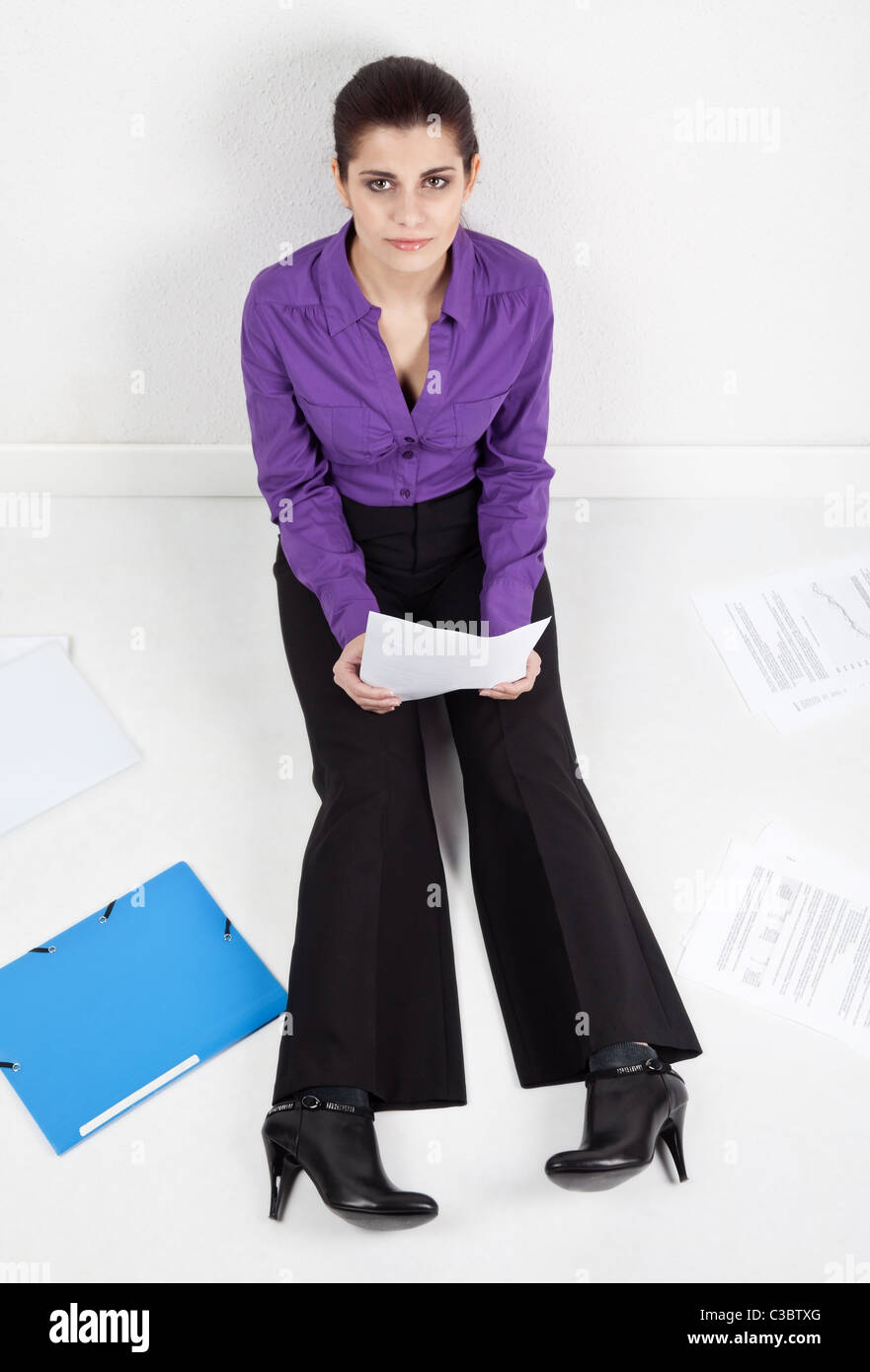 Young pretty secretary sitting on the floor with documents and folders scattered around Stock Photo