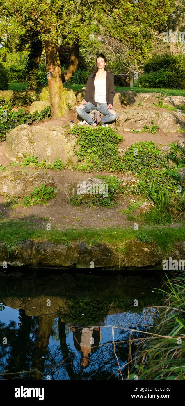Young woman doing yoga lotus position outdoor at Japanese gardens in Peckam Rye, London, England, Great Britain, UK Stock Photo