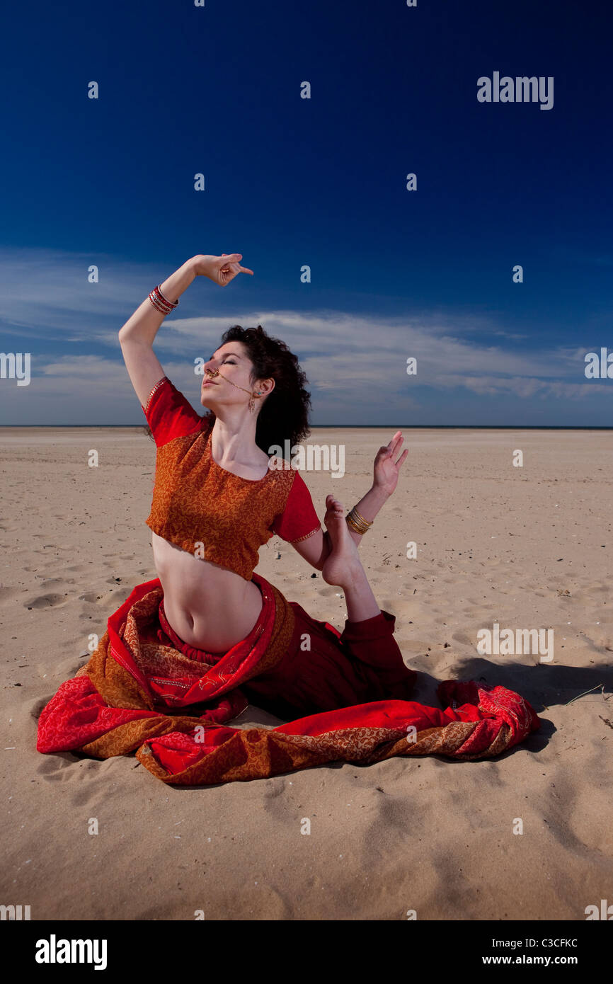 Beautiful young 'Belly Dancer' strikes pose against dramatic sky and beach in Indian clothing, UK. Bellydancer and yoga Stock Photo