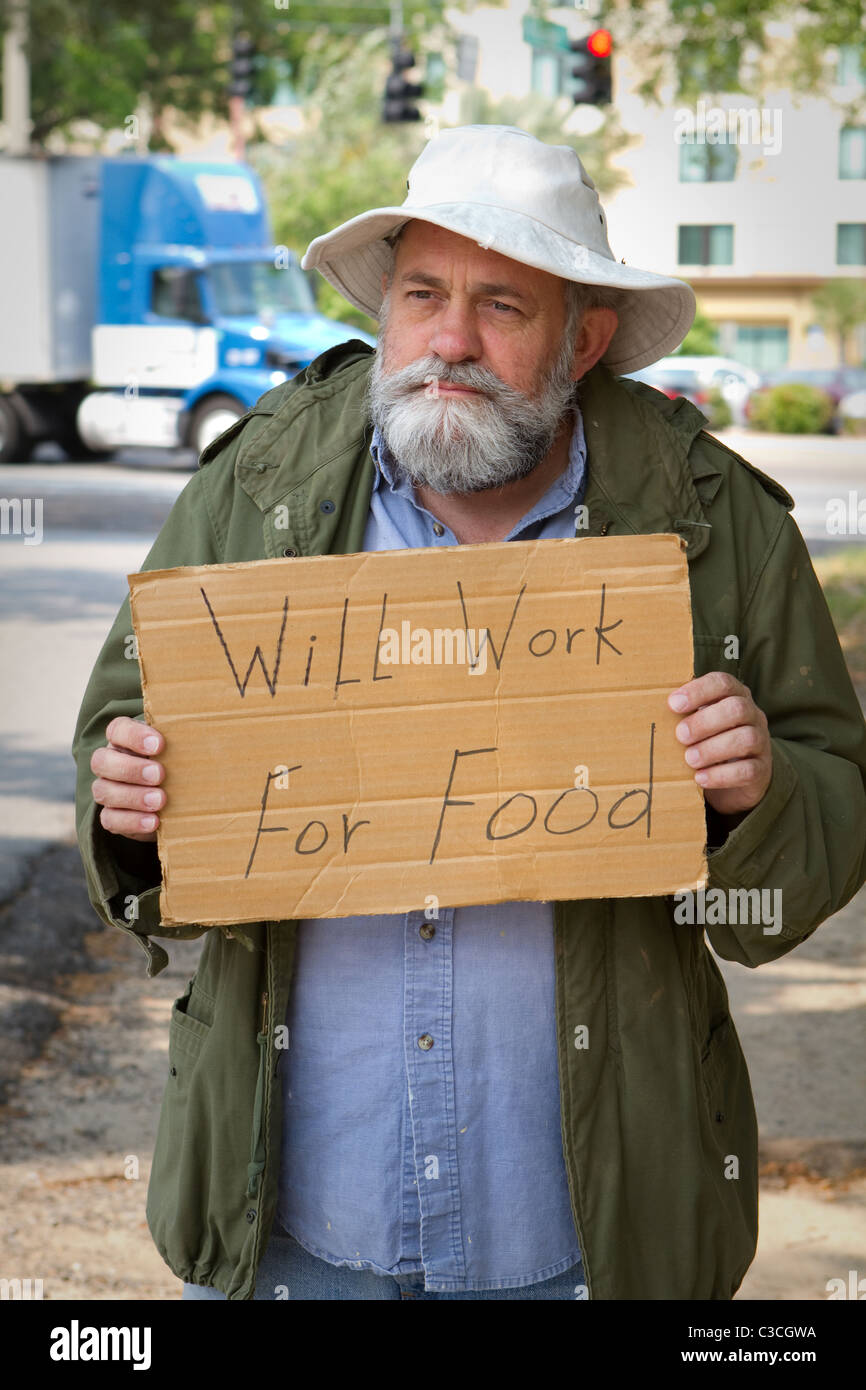 Homeless veteran begging at the side of the road holding a sign that says, 'Will Work For Food.' Stock Photo