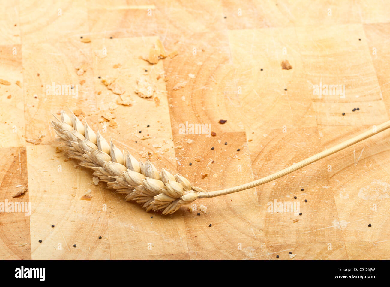 Dried ear of cereal crop on wooden bread board with crumbs and poppy seeds. Stock Photo
