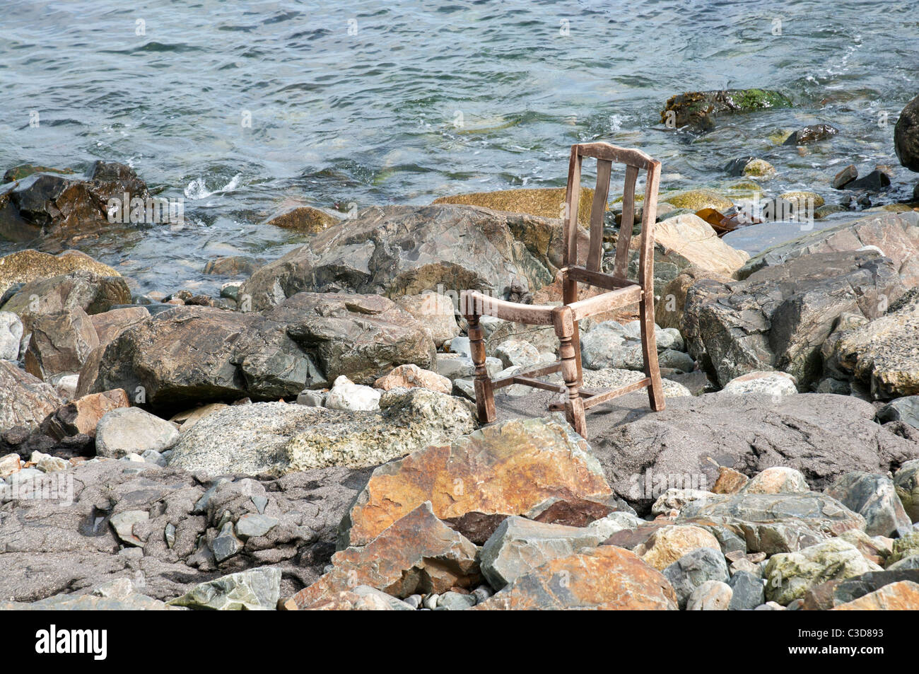 Abandoned broken wooden chair upright on stony beach near Newlyn