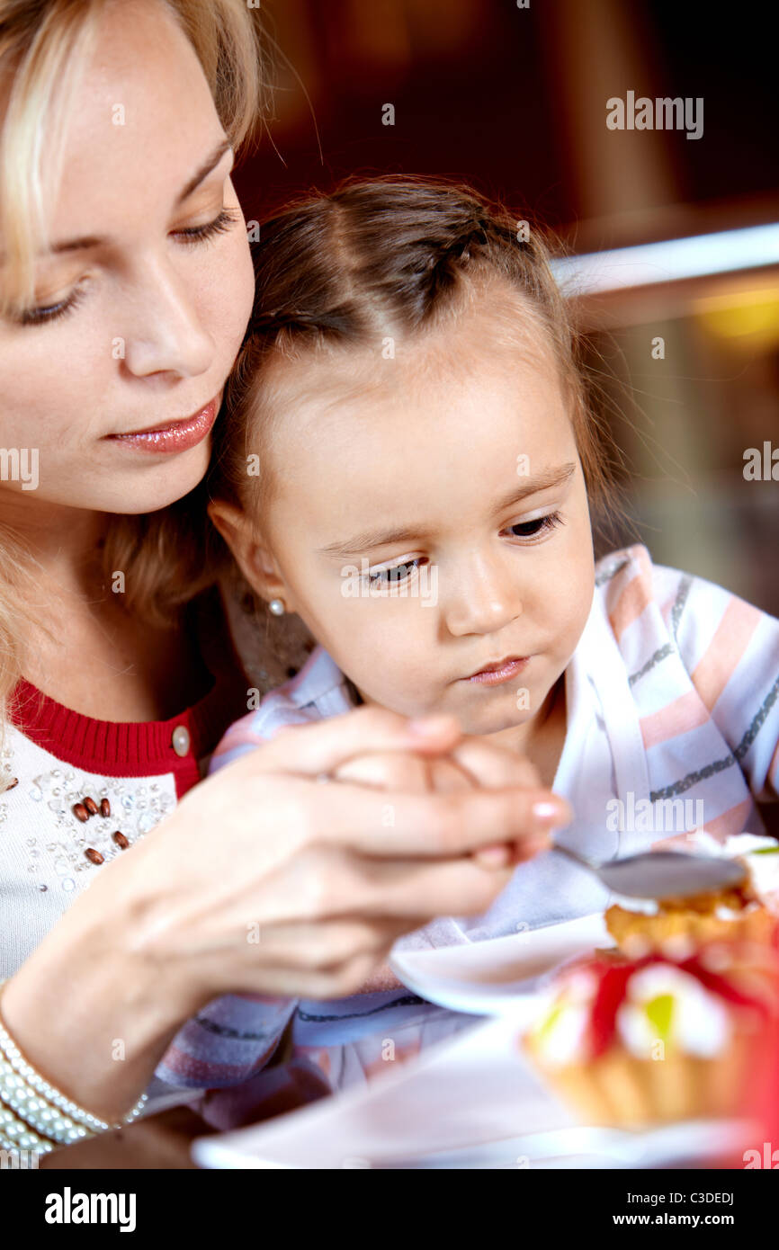 Portrait of cute girl eating cupcake with her mother near by in cafe Stock Photo
