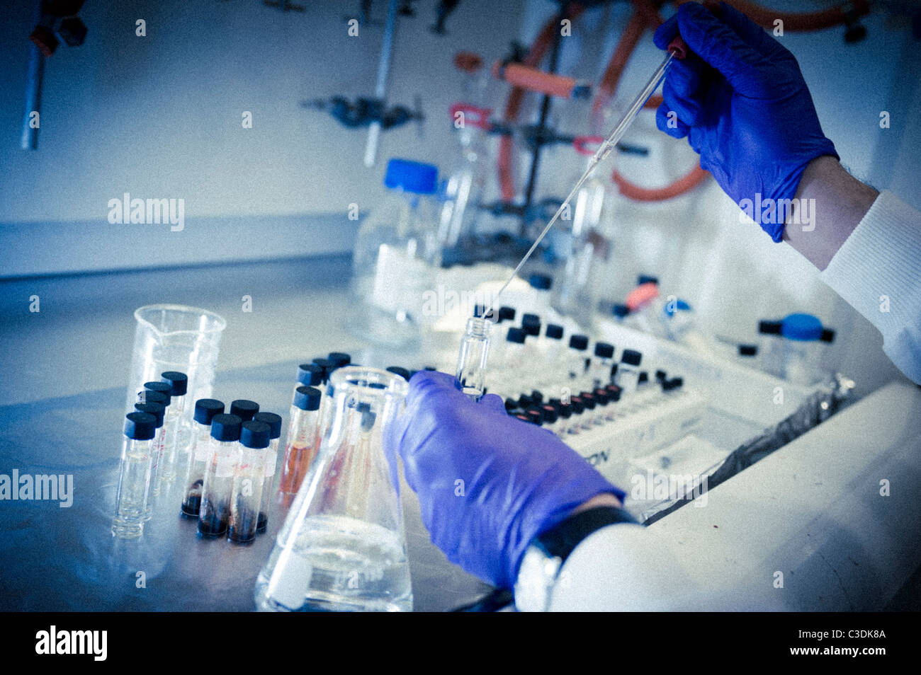 Close up of male scientist wearing white lab coat goggles and purple gloves working at fume cupboard with pipette and flasks Stock Photo