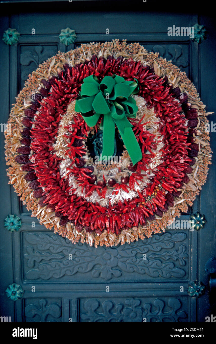 A traditional Southwestern Christmas holiday wreath hanging on an old carved wooden door features dried red chili peppers in Santa Fe, New Mexico, USA. Stock Photo