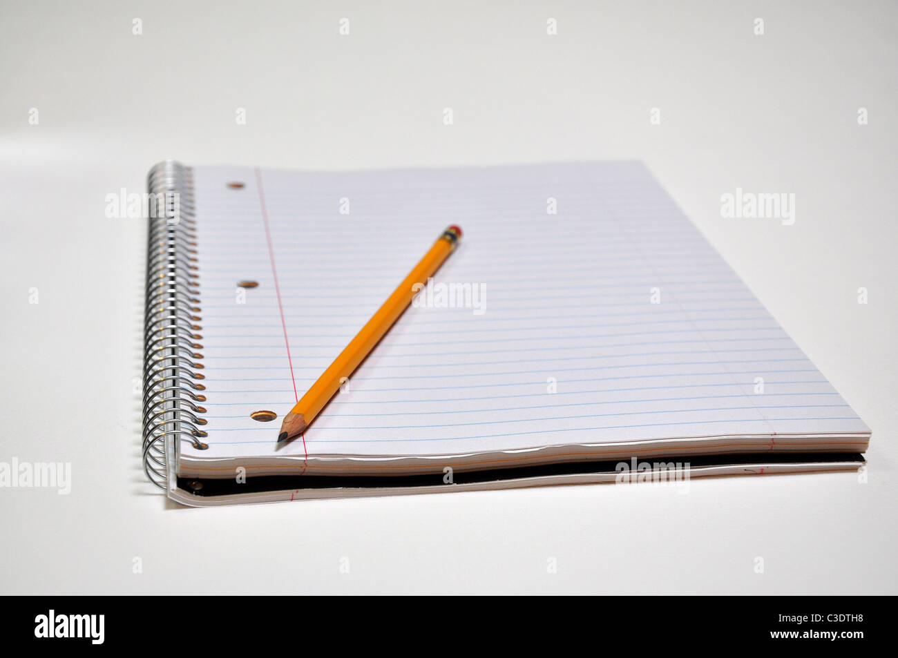 A standard size notebook with a pencil is sitting on a white background with shallow depth of field. Stock Photo