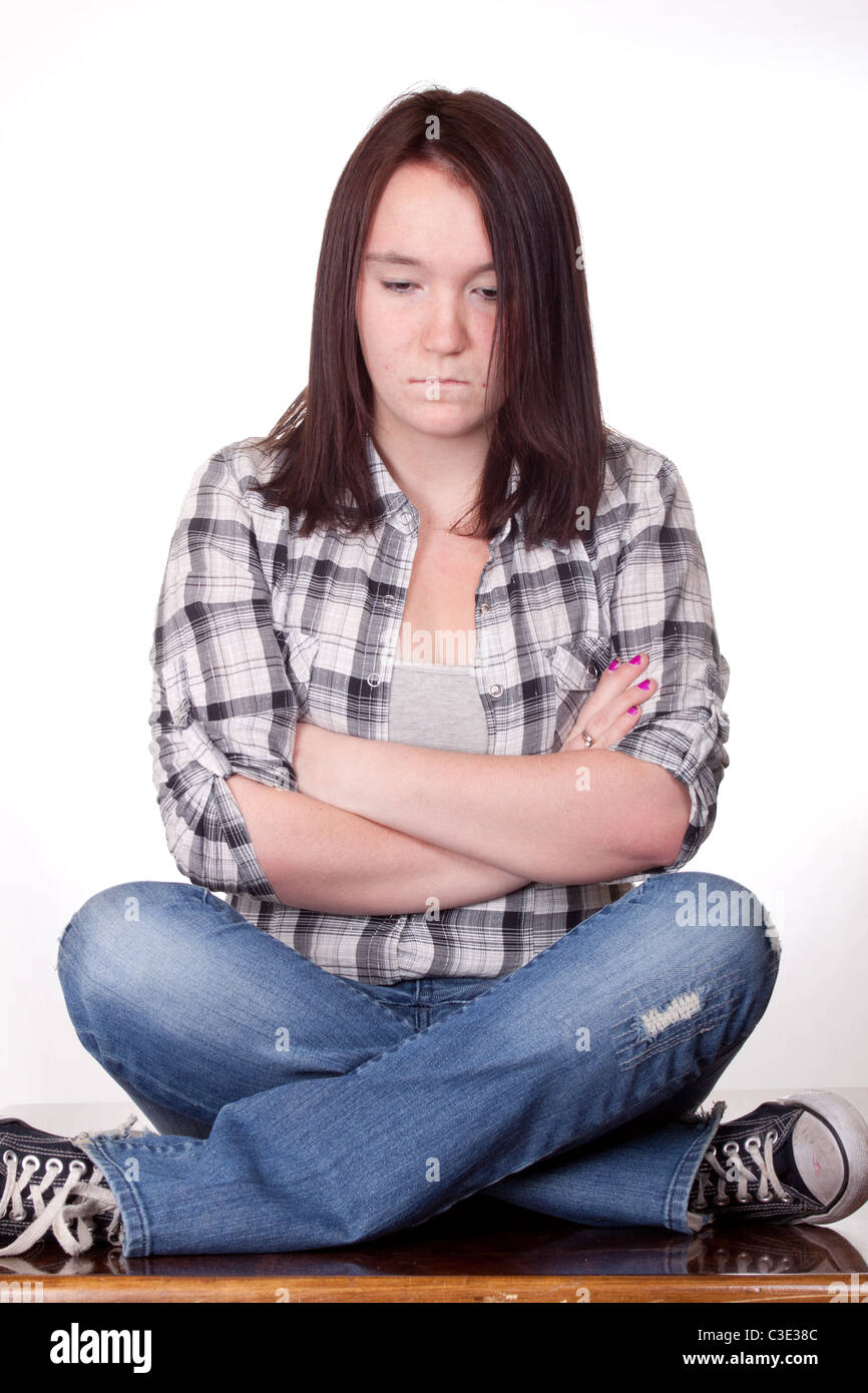 A photograph of a teenage girl sitting with her legs and arms crossed pouting. Stock Photo
