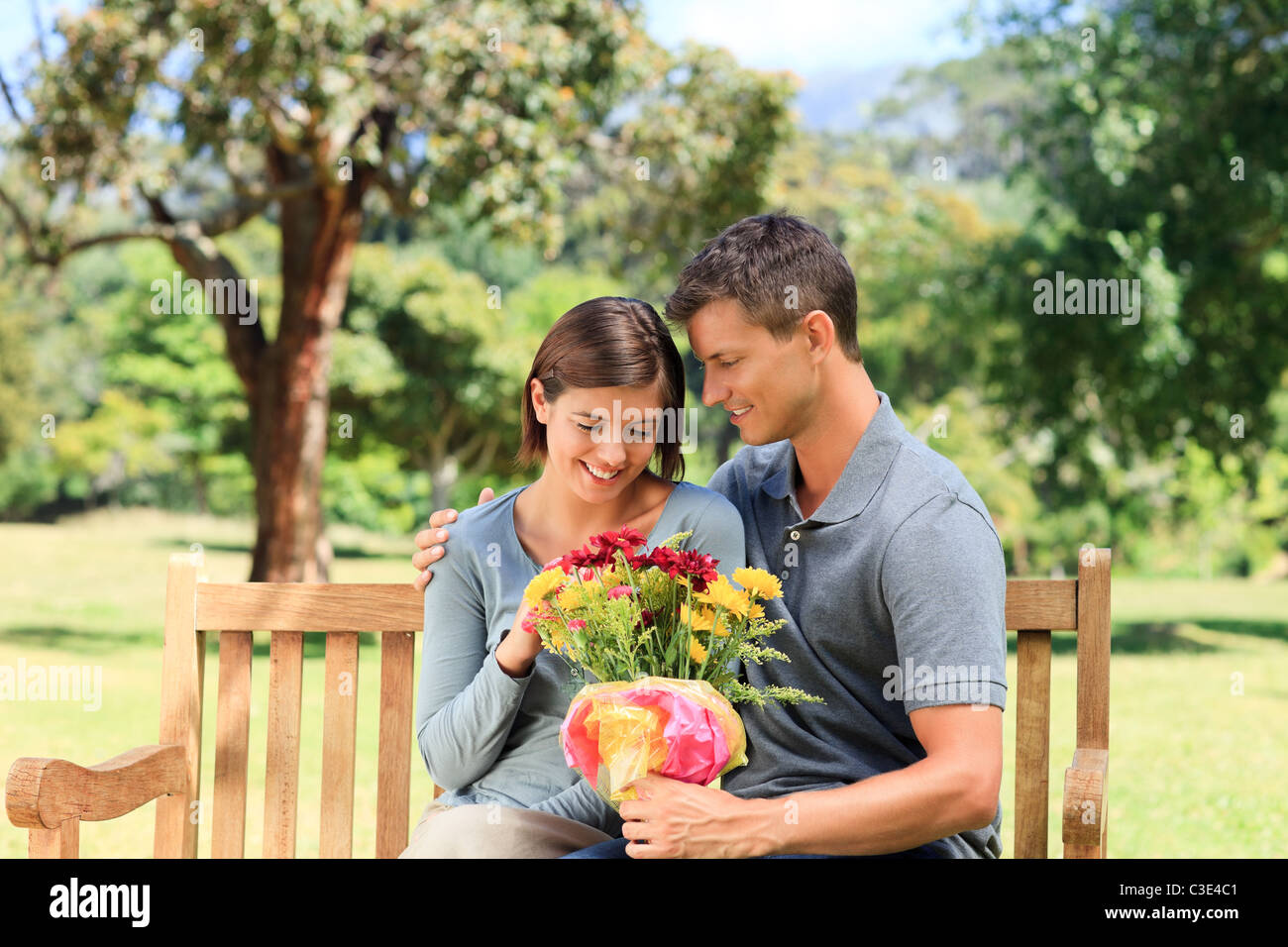 Man offering flowers to his girlfriend sitting on a bench Stock Photo