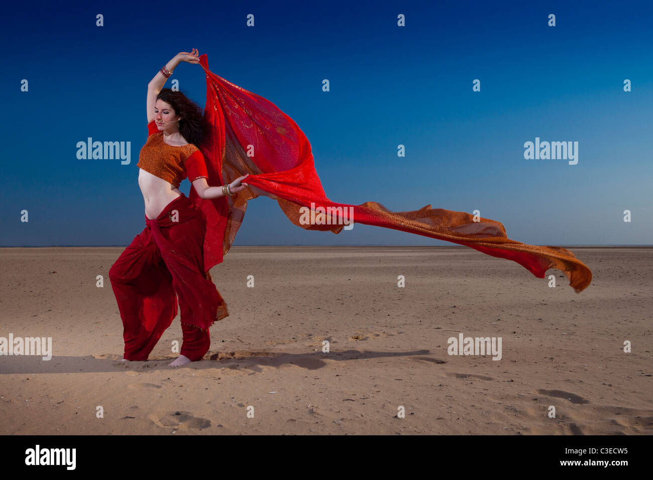 Beautiful young 'Belly Dancer' strikes pose against dramatic sky and beach in Indian clothing, UK. Bellydancer and yoga Stock Photo