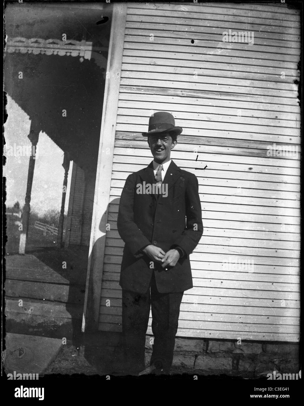 man in tall hat standing next to wooden house porch architecture home 1890s suit fashion Stock Photo