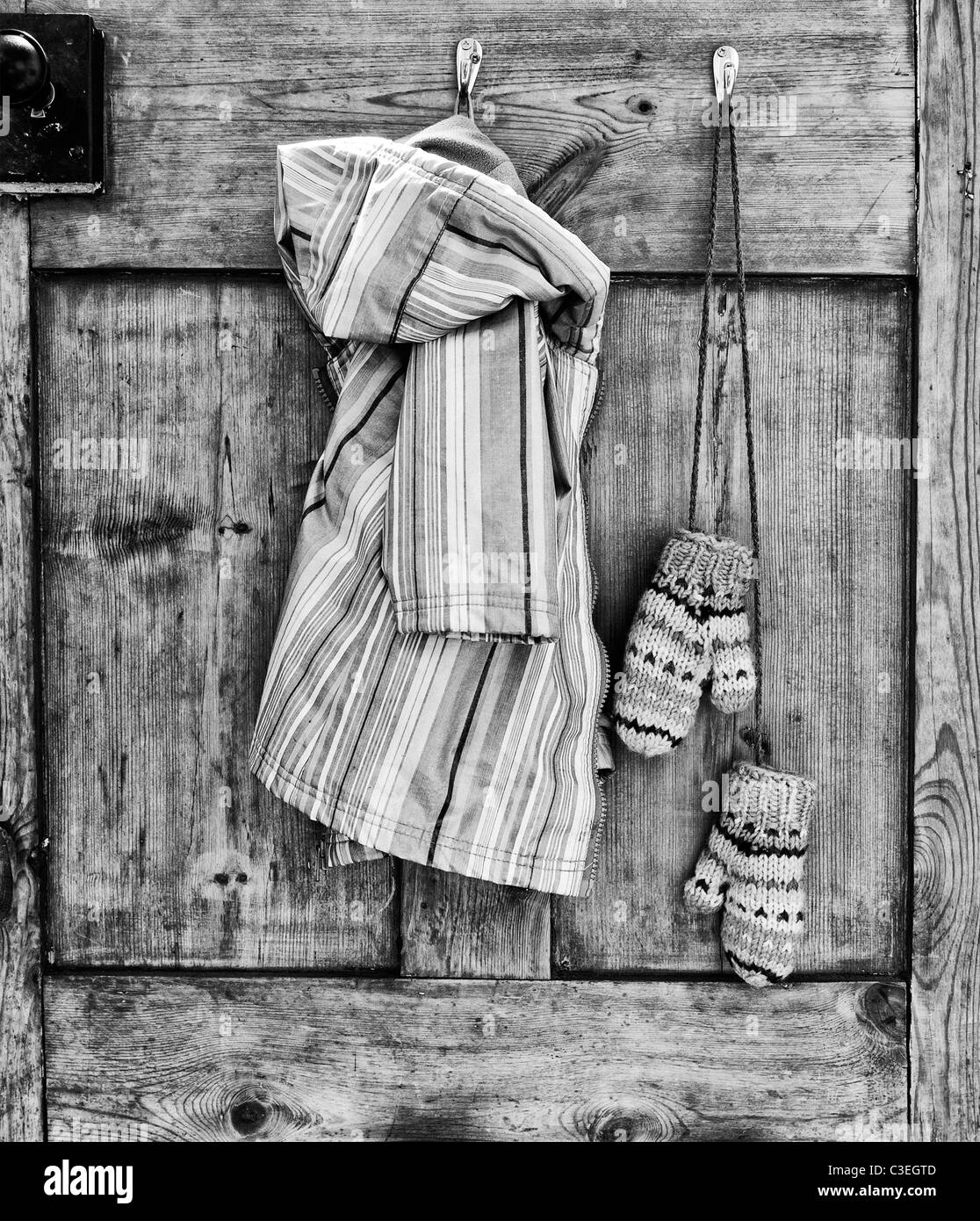 Young Girls striped coat and mittens hanging on a wooden kitchen door. Monochrome Stock Photo