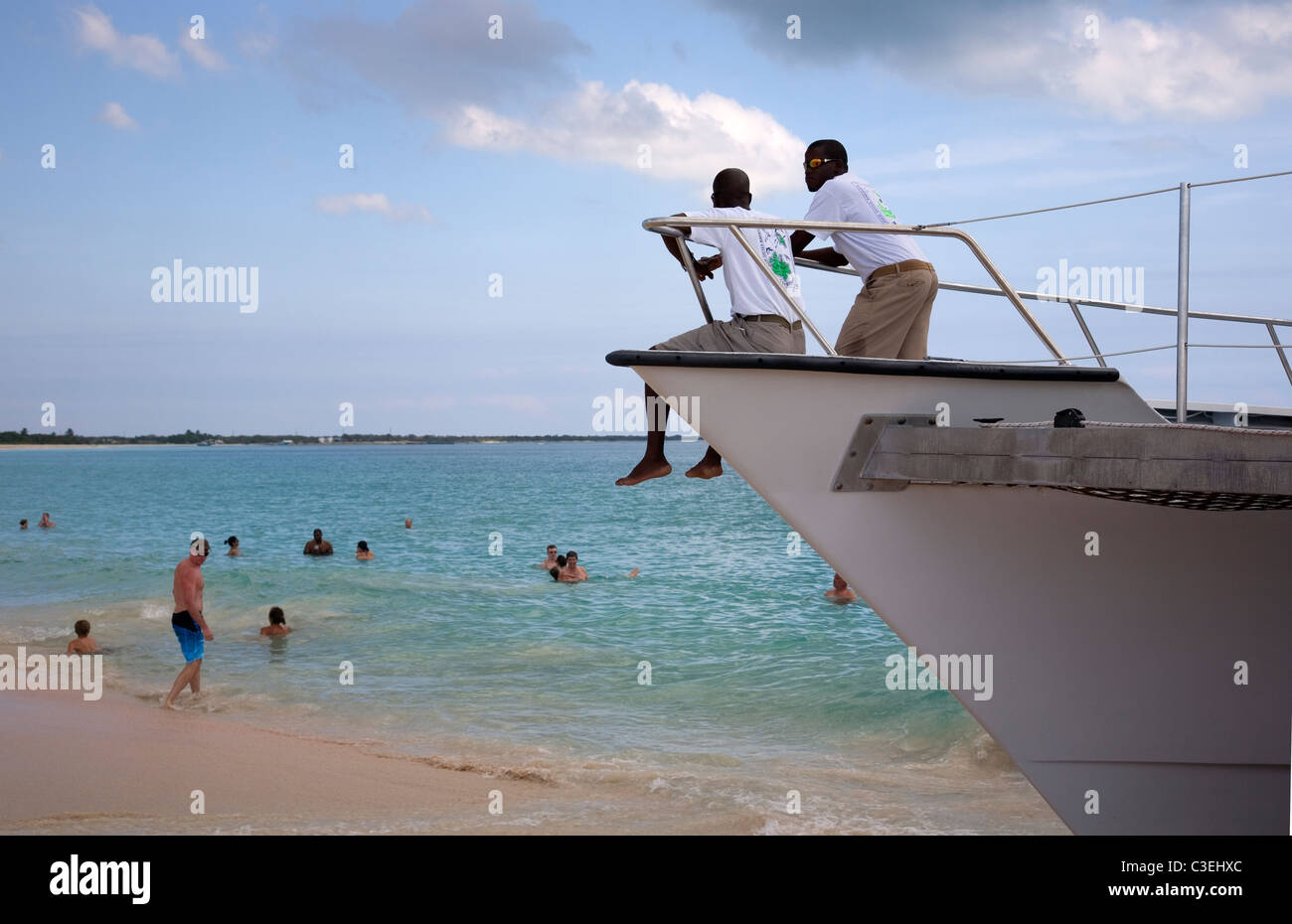 Two Cruise guides look on as tourists bathe in ocean in Barbuda - River Landing Beach Stock Photo