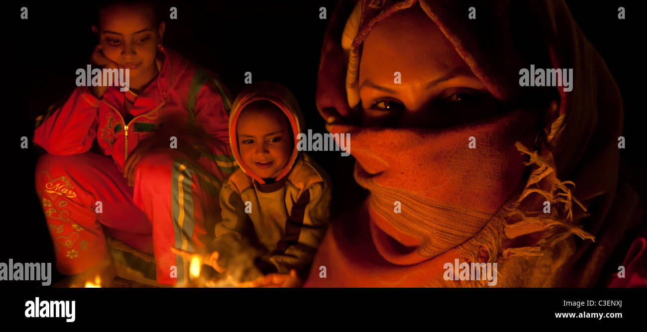panoramic portrait of young woman with two younger girls behind sitting in the glow of an outdoor fire, Egypt Stock Photo