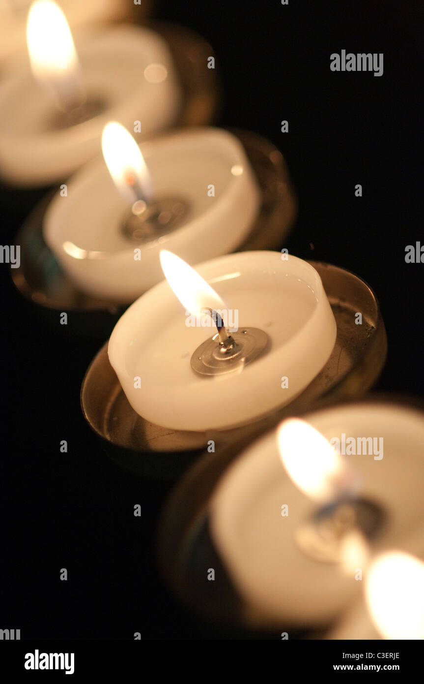 A row of burning votive candles with a black background Stock Photo