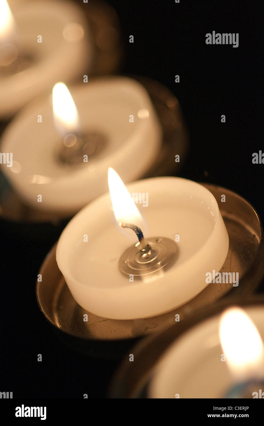 A row of burning votive candles with a black background Stock Photo - Alamy