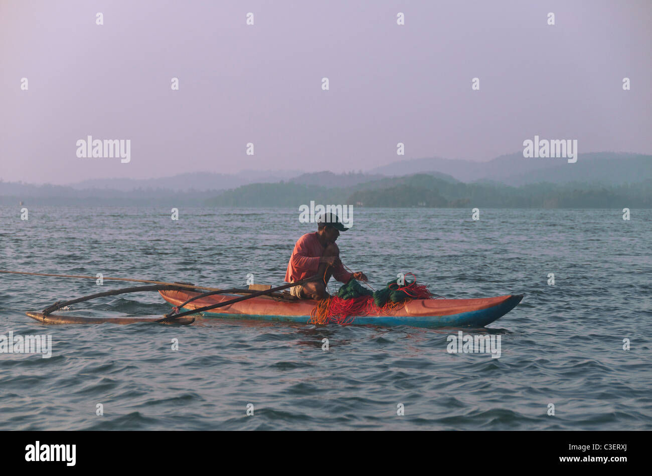Fisherman in outrigger canoe pulling in nets Koggala Lake Southern Sri Lanka Stock Photo