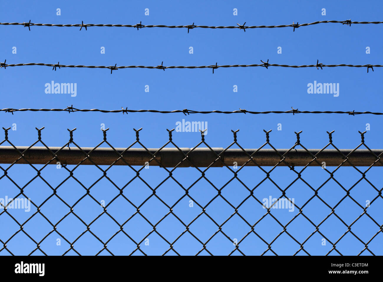 chain link and barbed wire fence top with blue sky background Stock Photo