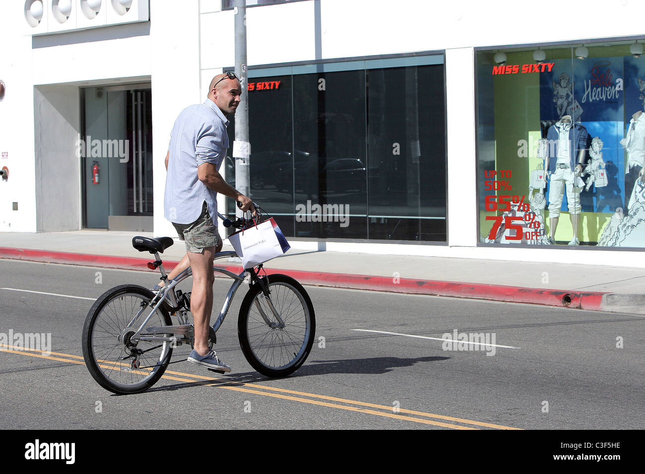 Billy Zane, wearing very short cut off shorts, rides his bicycle as he ...