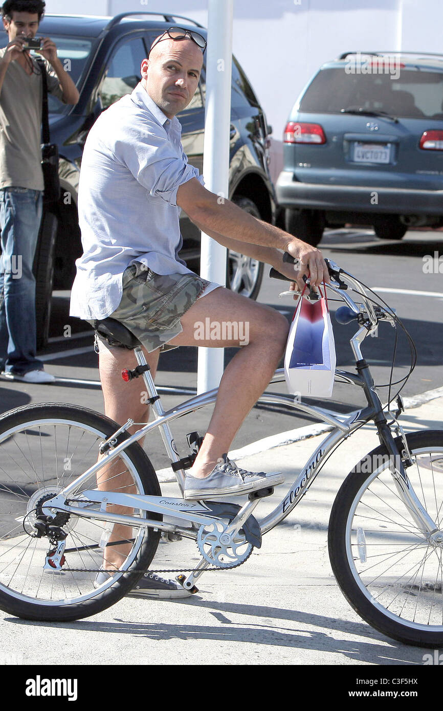 Billy Zane, wearing very short cut off shorts, rides his bicycle as he ...