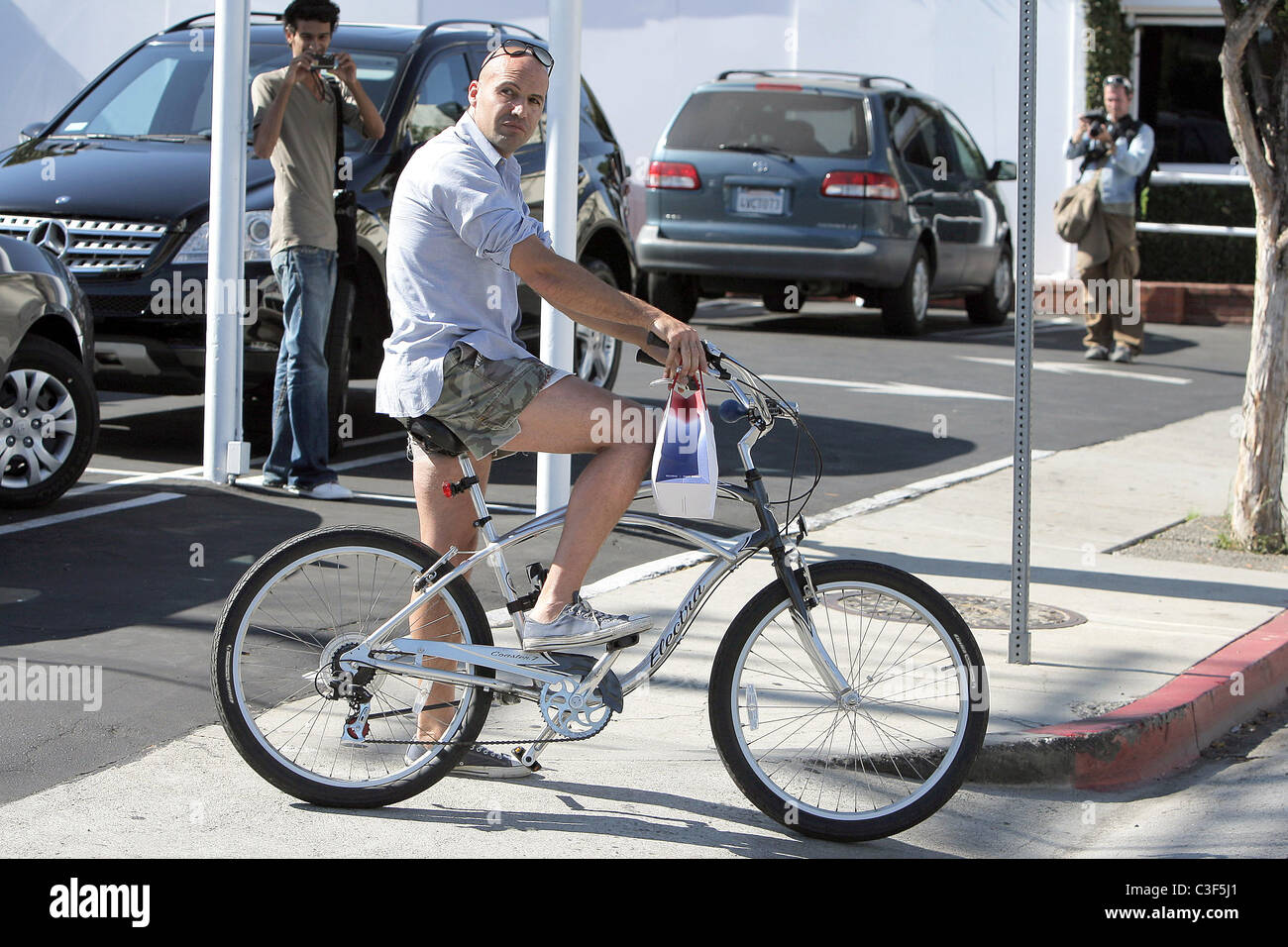 Billy Zane, wearing very short cut off shorts, rides his bicycle as he ...