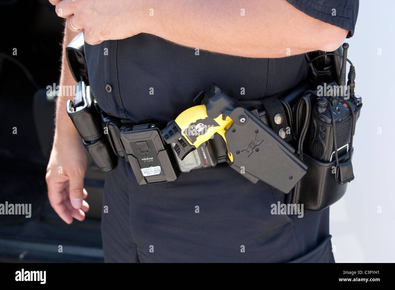 Police officer's duty belt includes a yellow Taser 'stun gun' in a holster. Stock Photo