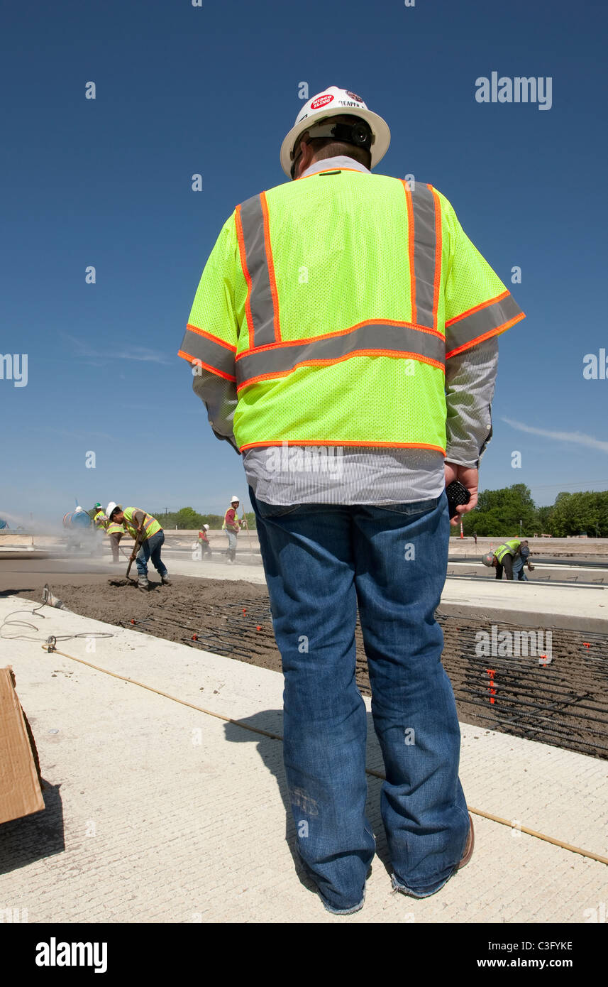 Male construction worker supervisor  wearing safety vest oversees crew working on new stretch of highway in Austin, Texas Stock Photo