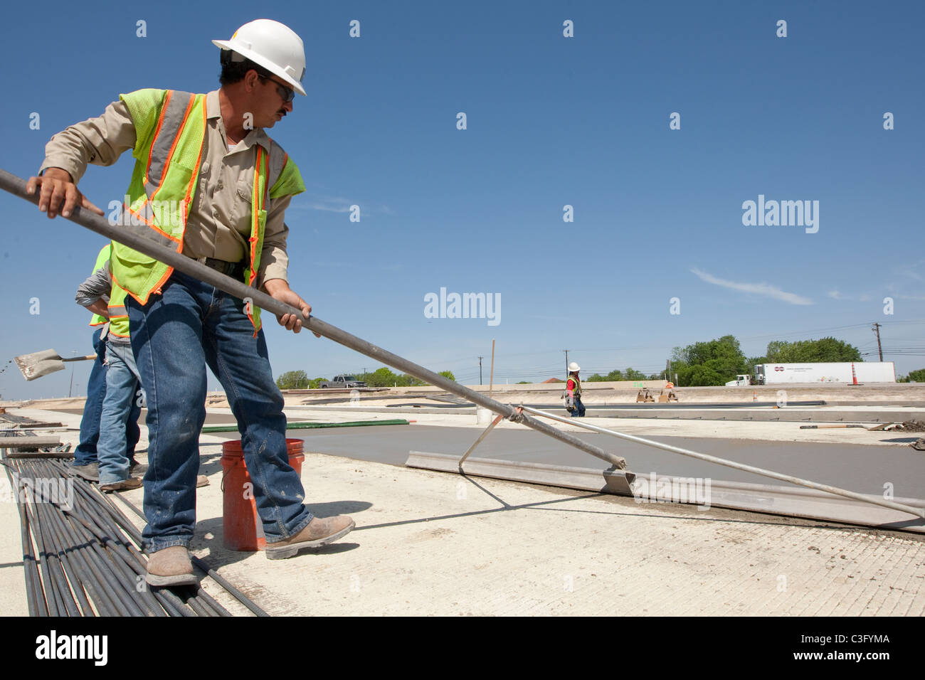Texas highway construction worker smooths out freshly poured concrete with large trowel on stretch of road in Austin, Texas Stock Photo
