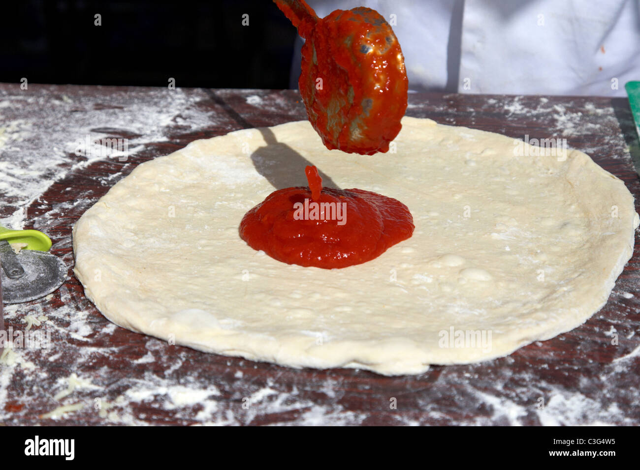 adding tomato sauce to pizza base to make fresh pizza Stock Photo