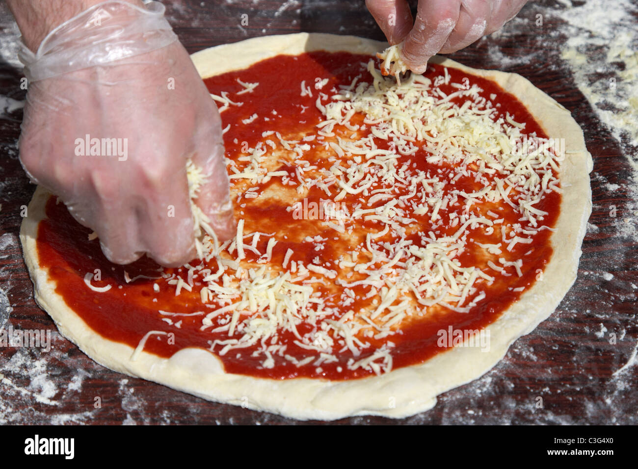 spreading cheese over tomato sauce and pizza dough base to make fresh pizza Stock Photo