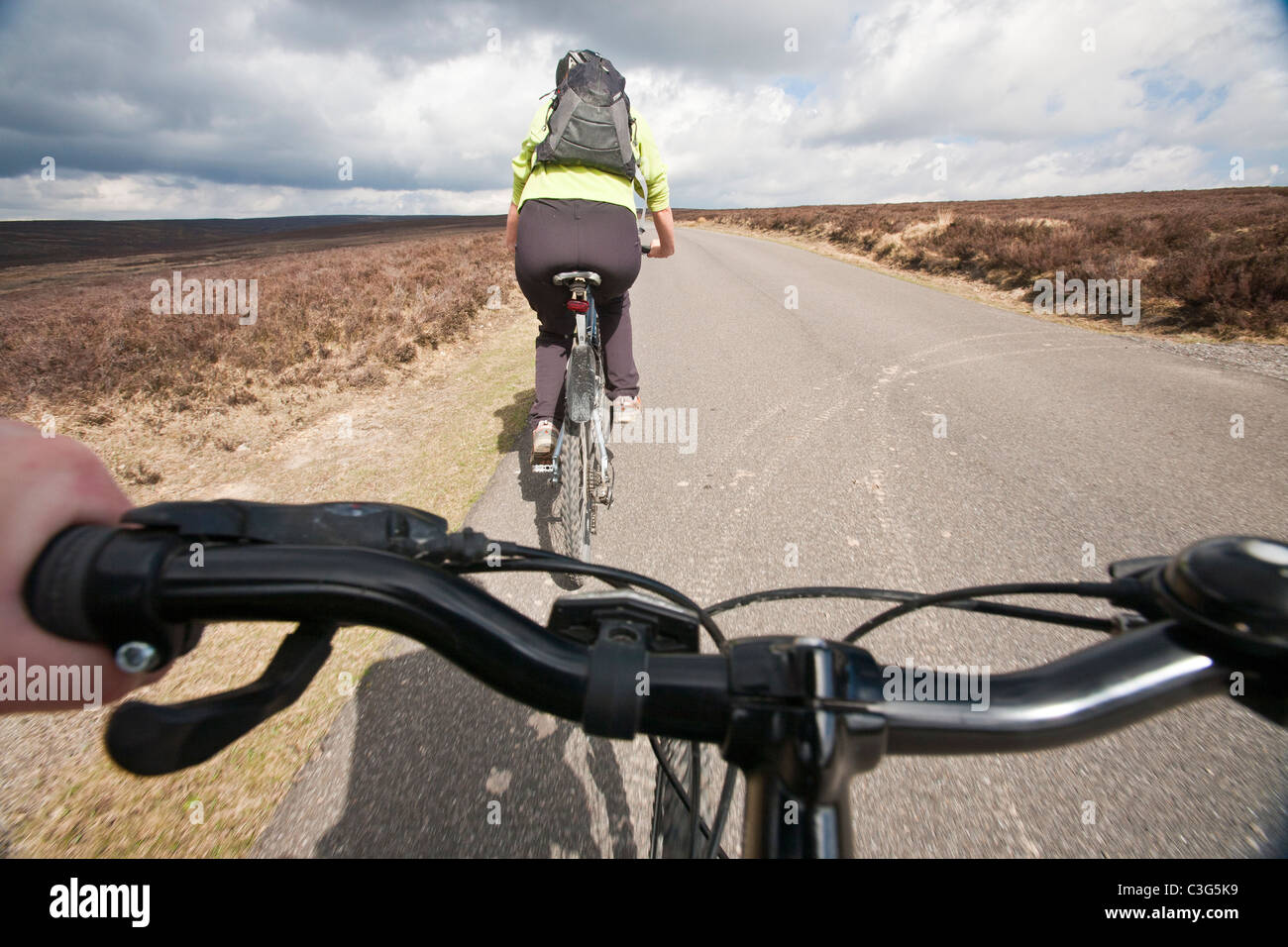 A woman mountain biking over the North York Moors road from Hutton-le-Hole to Rosedale. Stock Photo