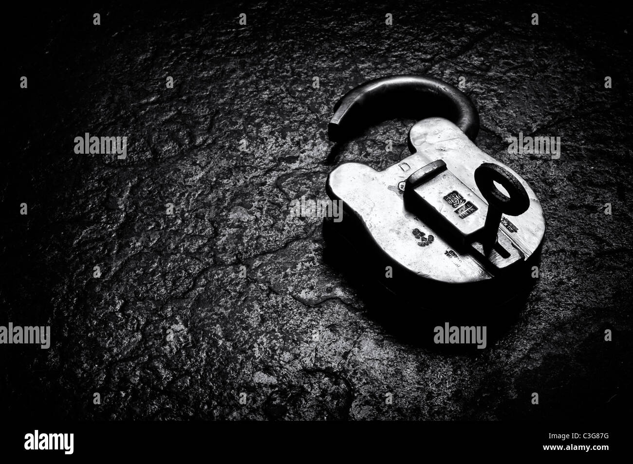 Old brass padlock and key on slate lit up by sunlight. Monochrome Stock Photo