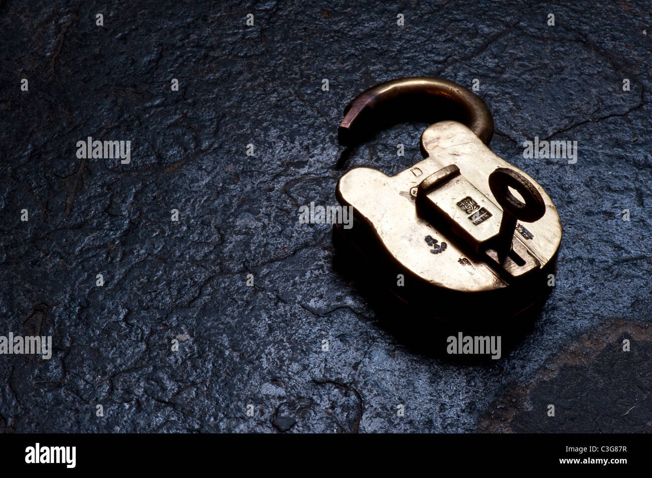 Old brass padlock and key on slate lit up by sunlight Stock Photo