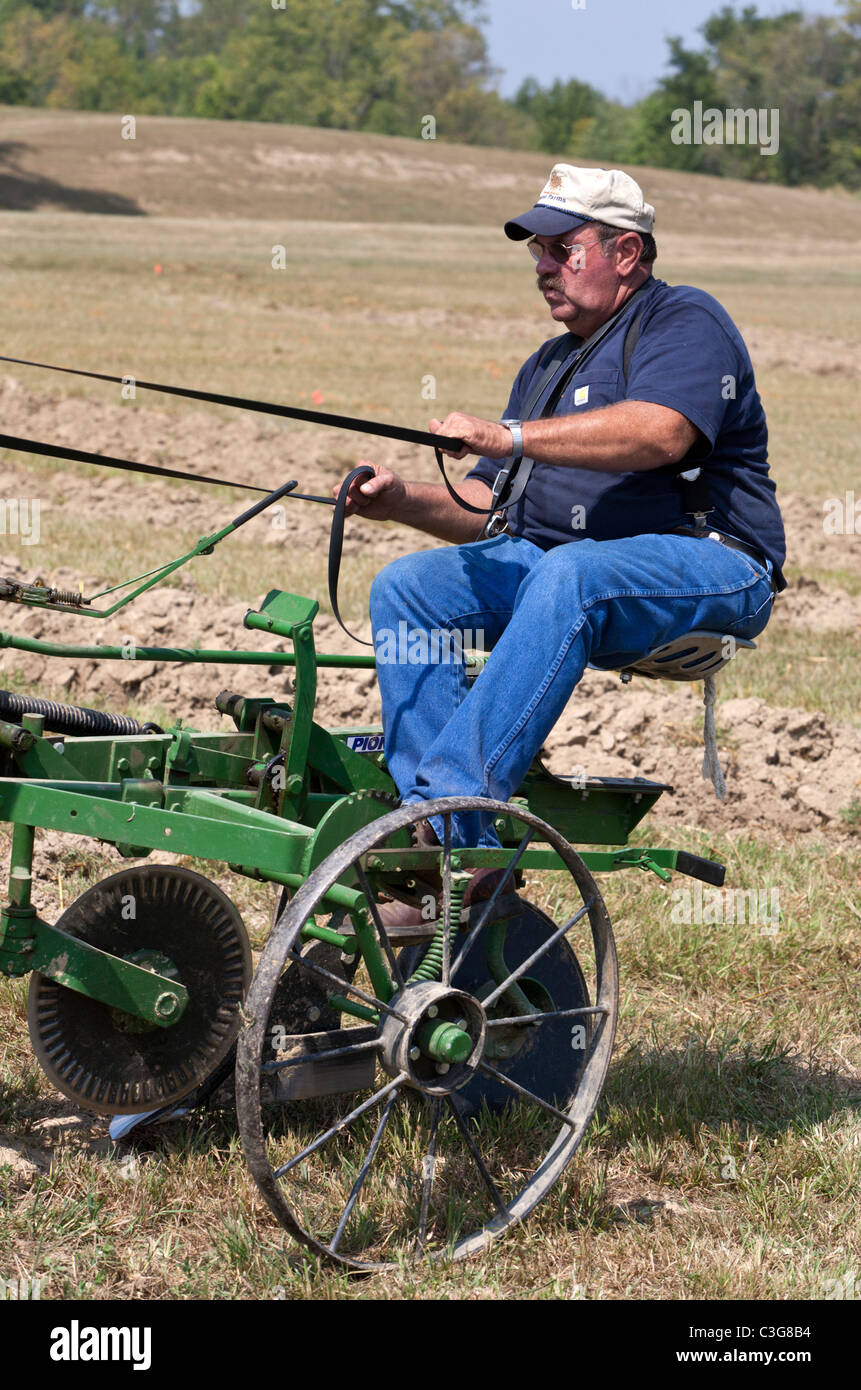 Man sitting on the back of a plow while preparing a field for planting